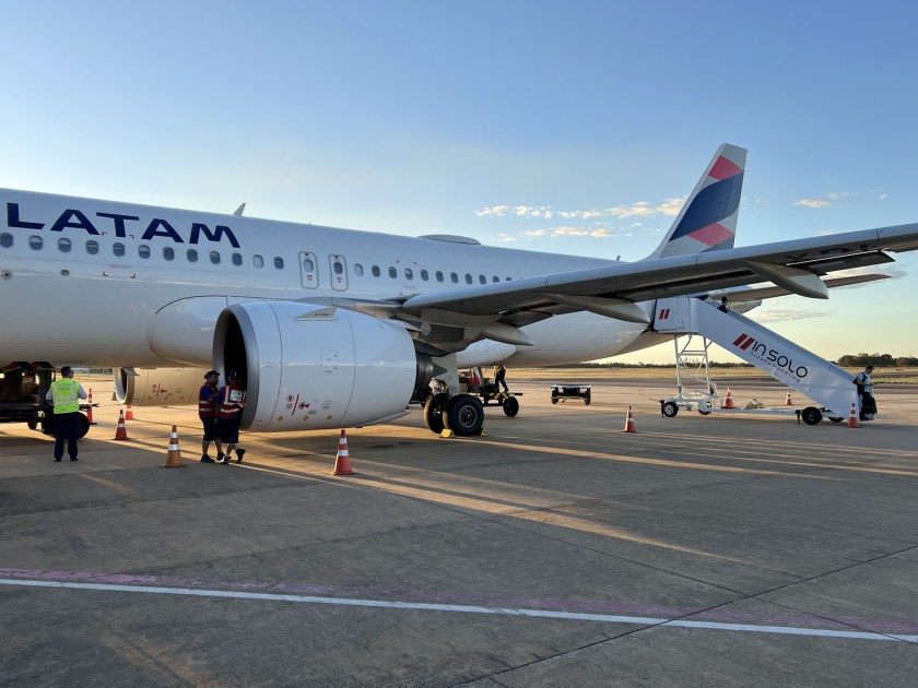 Avião da Latam parado na pista de uma aeroporto em dia de céu azul.