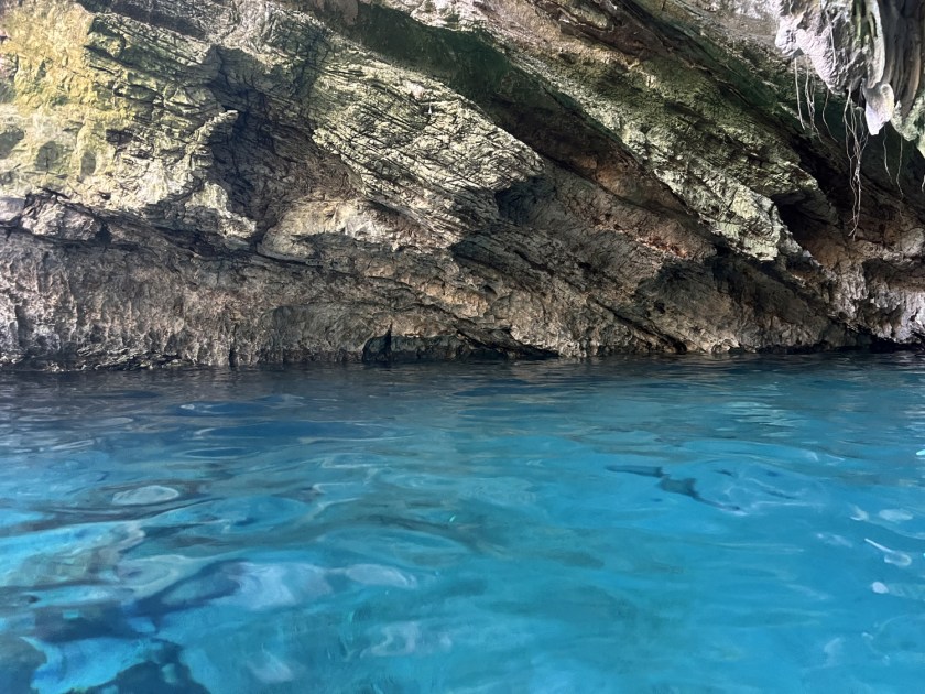 Foto com água da lagoa transparente e azul na metade inferior e rocha na parte superior.