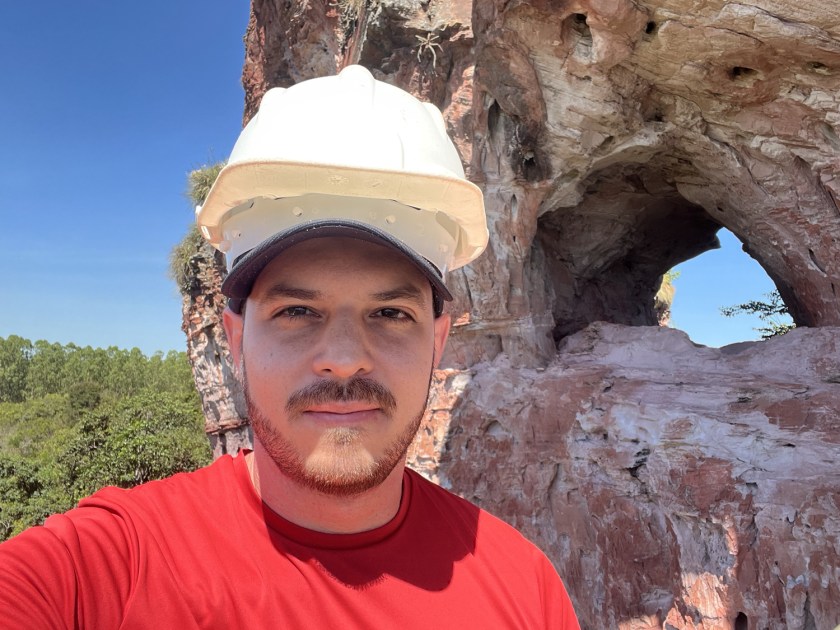 Homem com capacete de proteção branco e formação rochosa ao fundo.
