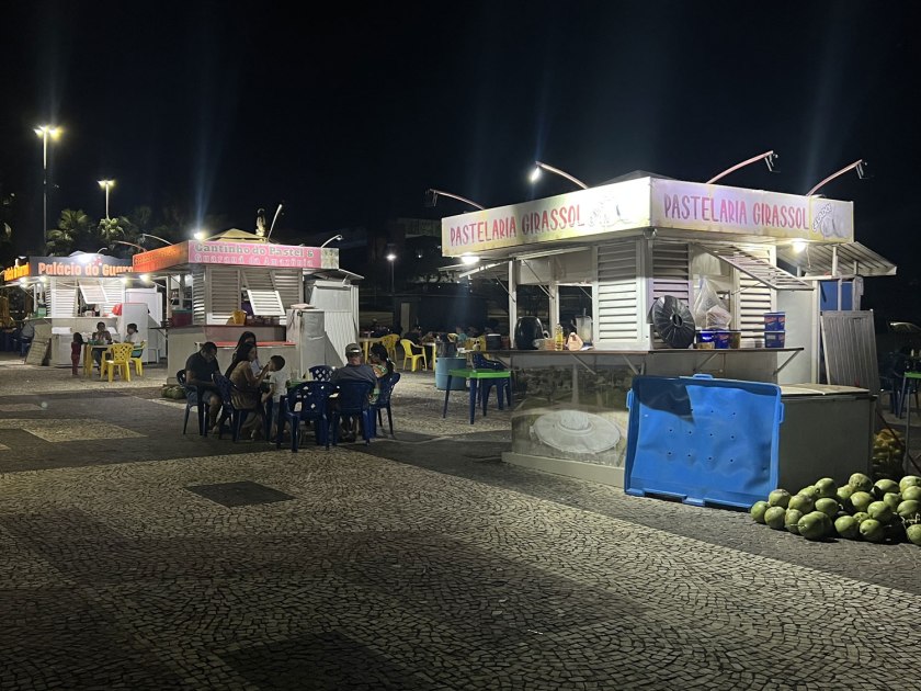 Quiosques de alimentação na praça com algumas pessoas sentadas durante a noite.