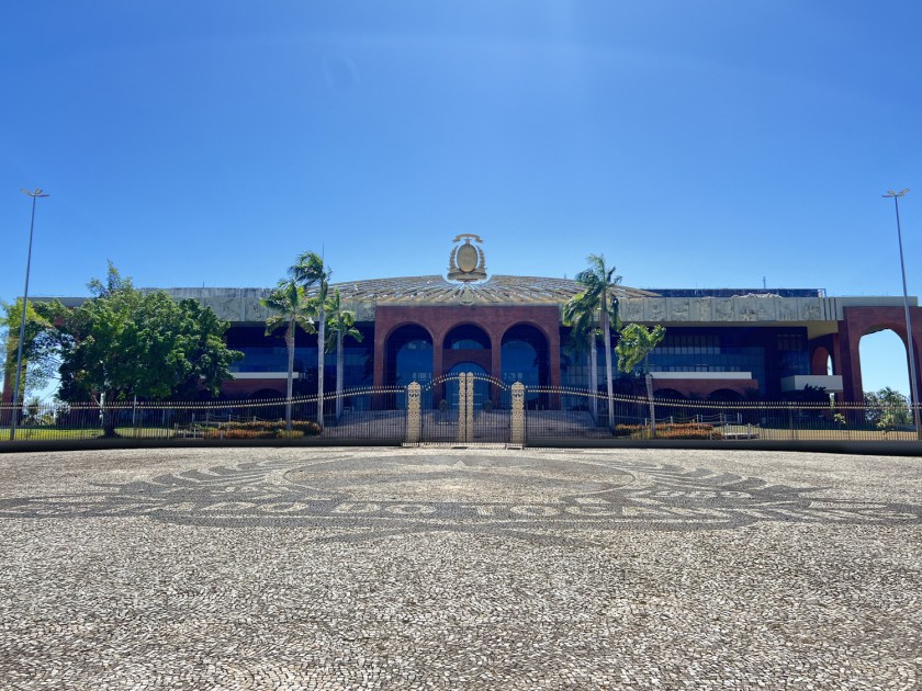 Praça com piso português formando brasão no chão com palácio ao fundo.
