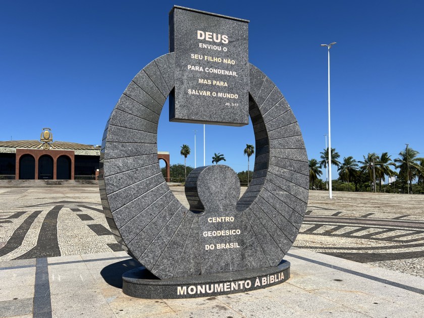 Monumento circular em praça com palácio ao fundo.