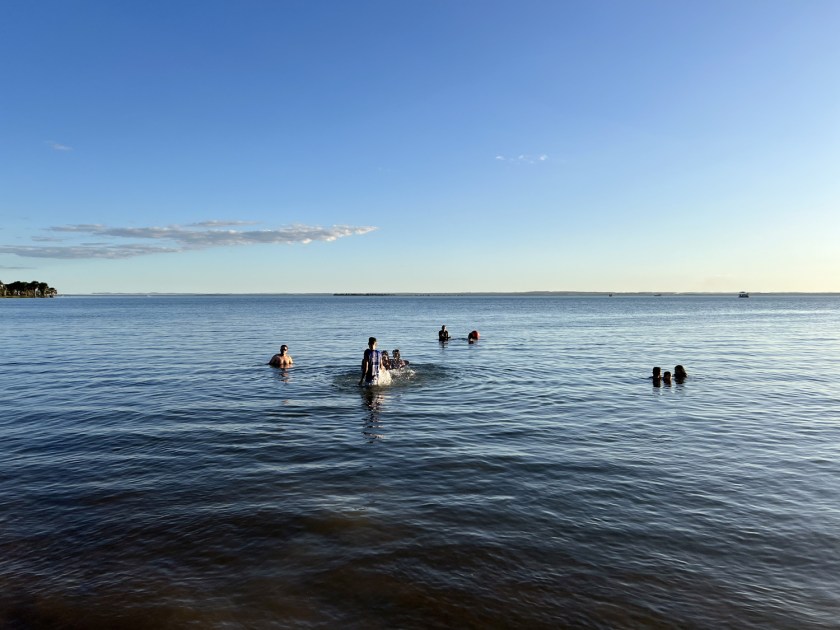 Pessoas nadando em lago com céu azul ao fundo.