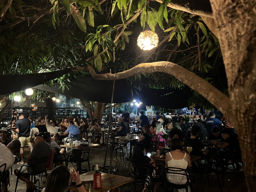Diversas pessoas sentadas num bar a noite com iluminação intimista.