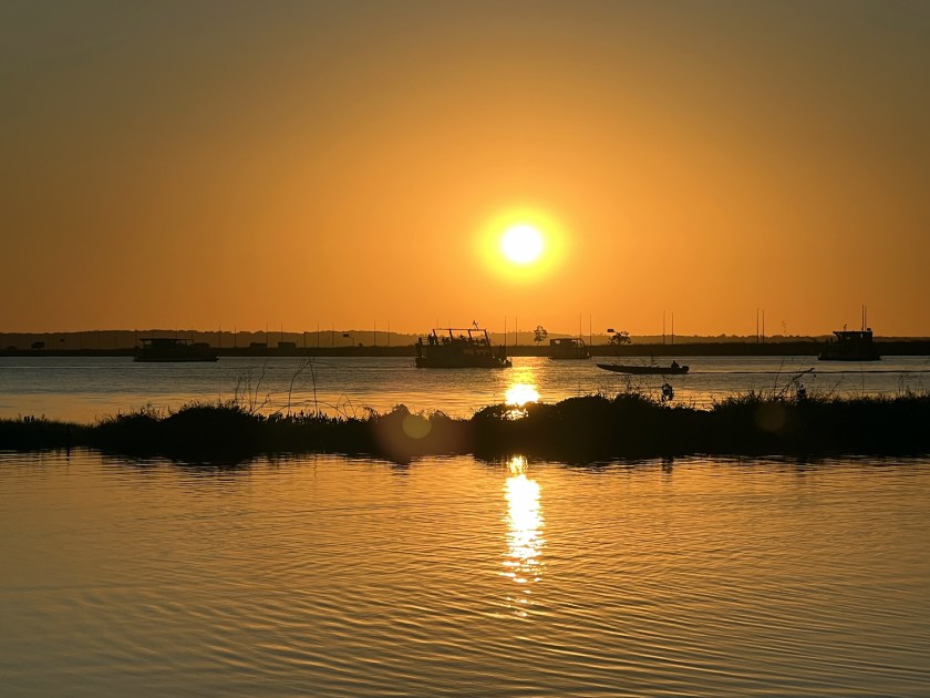 Pôr-do-sol em tons laranjas com reflexo na água do lago.