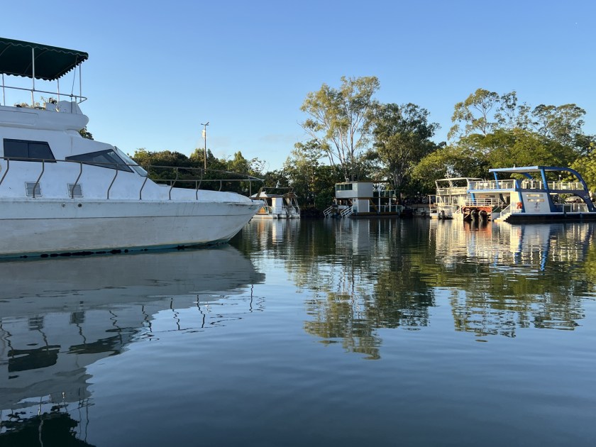 Embarcações ancoradas no porto com a água refletindo o céu.
