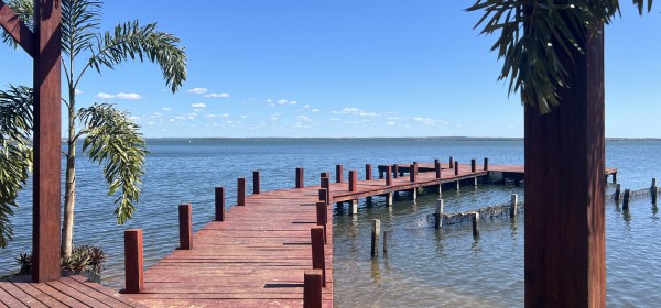 Deck de madeira pintada de vermelho nas águas calmas do lago com dia de céu azul.