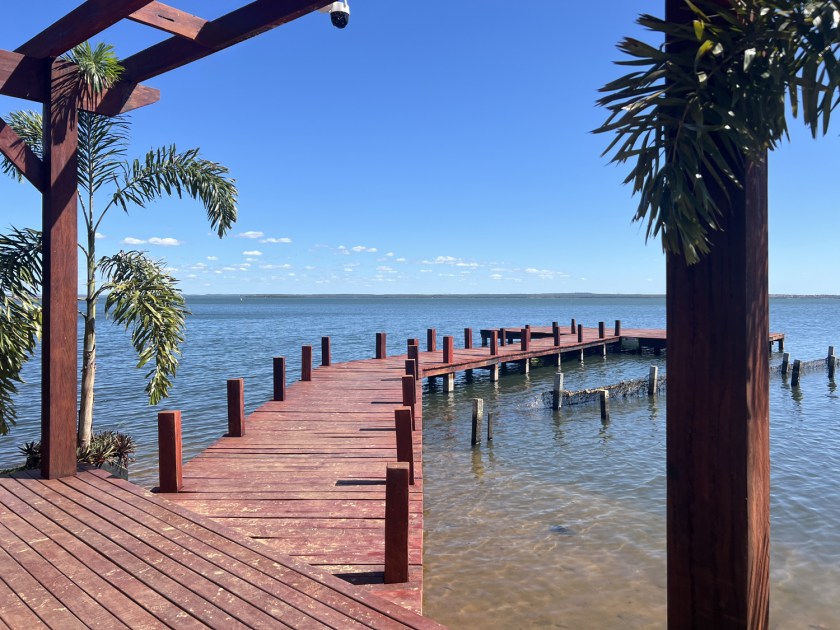 Deck de madeira pintada de vermelho nas águas calmas do lago com dia de céu azul.