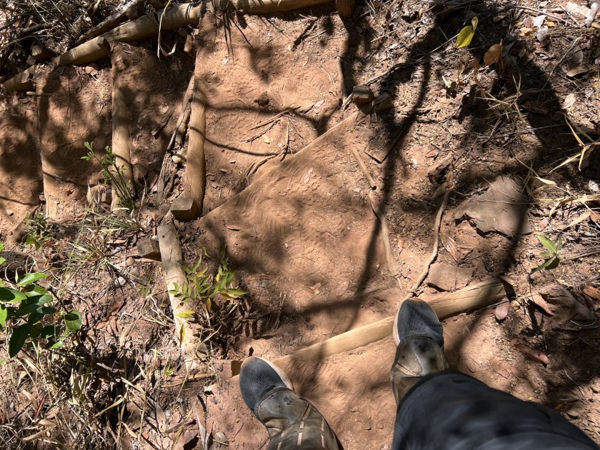 Descida por degraus em trilha de terra com estrutura de madeira.