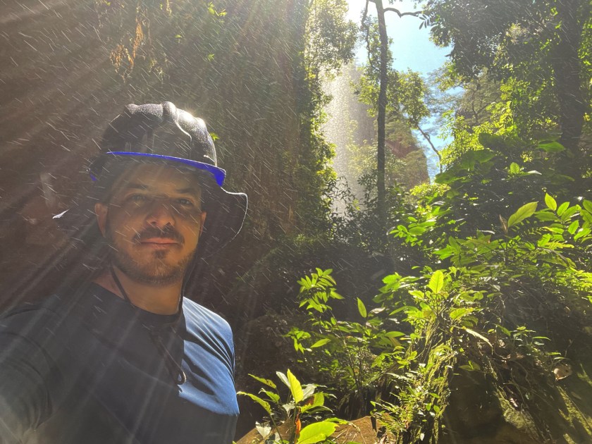 Homem com capacete de segurança sob vapor de cachoeira no fundo de um cânion.